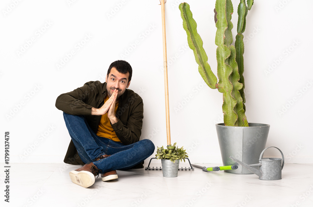 © luismolinero - Gardener man sitting on the floor at indoors keeps palm together. Person asks for something © luismolinero - Gardener man sitting on the floor at indoors keeps palm together. Person asks for something