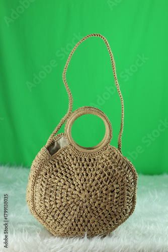 Crocheted cream bag on a white fluffy blanket in front of a green background.