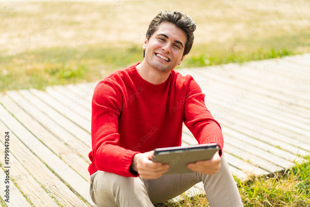 Obraz premium Young handsome man holding a tablet at outdoors with happy expression