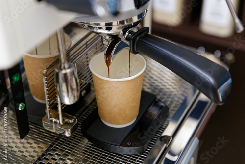 Closeup of espresso pouring from coffee machine in cardboard cup for take away. Shallow focus.