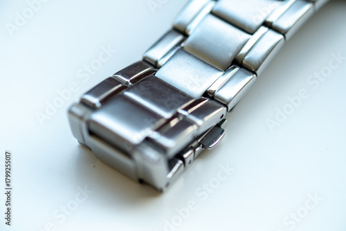 A high-angle macro view of a stainless steel watch bracelet, focusing on the brushed metal links and the deployment clasp, on a white surface.