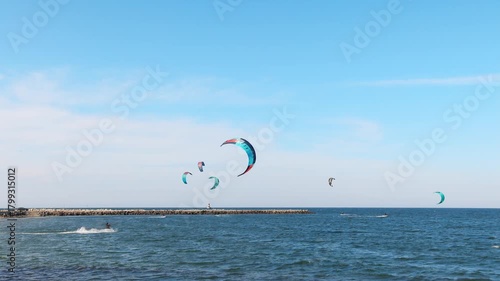 People in sportswear go kiting on the surface of the Black Sea near the town of Pomorie under a blue sky