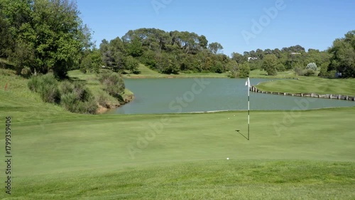 Golfer swings on sunny day at picturesque golf course near lake