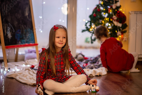 Two girls in red dresses are sitting near the New Year tree and looking for gifts