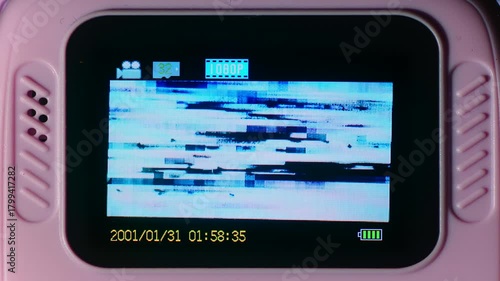 children's digital camera screen showing a heavily glitched video feed. The display features bright blue horizontal distortion lines, pixel noise