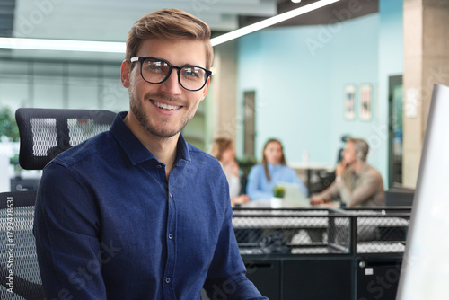 Good looking young business man looking at camera and smiling while sitting in the office.