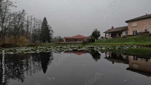 A small tranquil lake in a traditional French Alpine village near Lyon during autumn. Colorful fall foliage surrounds the calm water, creating a peaceful natural mountain landscape.
