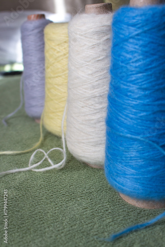 Variety colours of alpaca wool and silk. Cones of multicoloured yarn. Wool threads in a row. Row of blue, white, yellow and grey wool. Knitting hobby. Bobbins of yarn. Bright wool for knitting. 