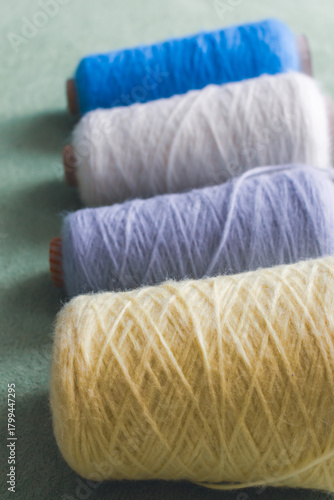 Variety colours of alpaca wool and silk. Cones of multicoloured yarn. Wool threads in a row. Row of blue, white, yellow and grey wool. Knitting hobby. Bobbins of yarn. Bright wool for knitting. 