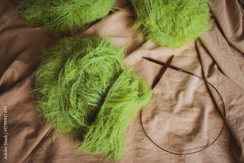 Green knitwear with wooden knitting needles on beige background. Knitting needles and fluffy knitting pattern. Knitted soft clothes with merino yarn ball and needles. Knitting hobby. Knitwear concept.