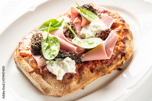 A gourmet Italian flatbread featuring mortadella, fresh ricotta cheese, and wild morel mushrooms, garnished with basil leaves on a white plate