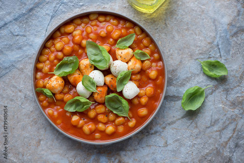 Mini potato gnocchi with tomato sauce and mozzarella on a blue and beige stone background, horizontal shot, top view