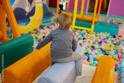 Fototapeta Naklejka Na Ścianę i Meble -  Child playing on cushioned rollers inside a bright indoor play area, with a large ball pit and soft equipment creating a fun and safe environment for early childhood activities