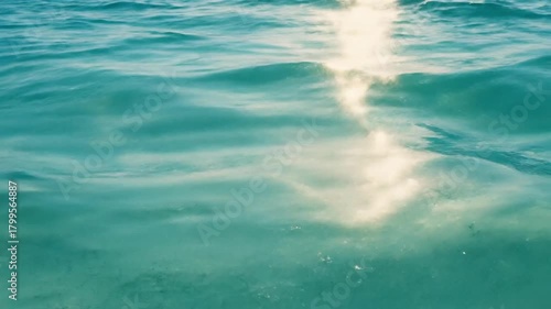 Glistening sunbeam dances on the serene, crystal clear teal water of the sea on a bright summer day