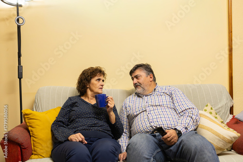 Mature couple talking on sofa enjoying coffee at home