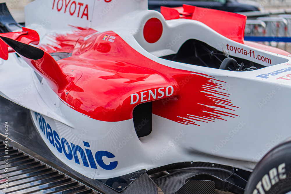 Naklejka premium Indoor shot of a red Toyota F1 car TF-108 with white accents and black stripes, featuring brand logos for Toyota, Denso, and Sony Prepared for dry conditions with s - Kyiv, Ukraine 10-10-2024