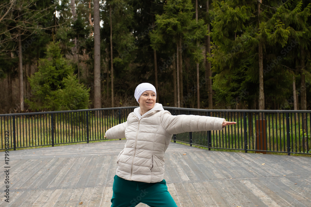 Fototapeta premium Bald woman with cancer practicing yoga outdoors in park, concept of recovery, self-care, and physical rehabilitation after chemotherapy.