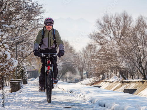 A man rides a bicycle on an icy sidewalk on a winter day. Active lifestyle in winter