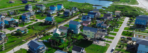 Panorama view grid of stilt vacation homes with grassy vacation land, Galveston, TX. Green space and paved drives support drainage, aesthetics, reflecting thoughtful coastal-suburban integration