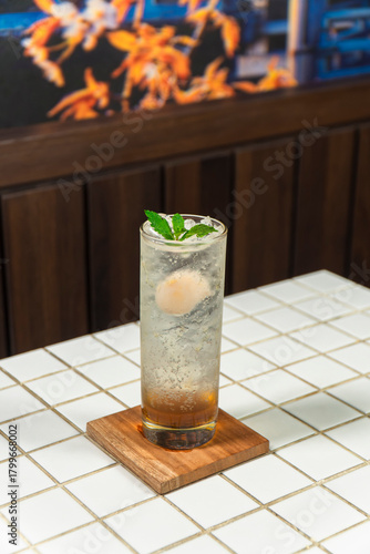 Fényképezés Refreshing Lychee Soda: A tall glass of sparkling lychee soda, garnished with a fresh mint sprig and a whole lychee, sits on a coaster, ready to quench your thirst