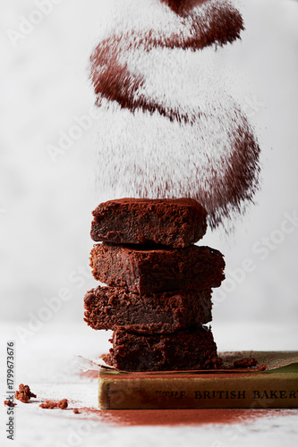 Stacked Chocolate Brownies with Falling Cocoa Powder on Light Background