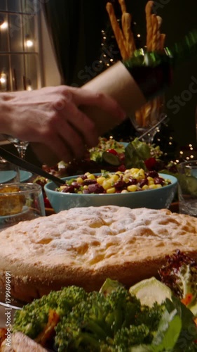 Vertical slow motion video camera moving over festive dinner table hands serving salad pouring wine warm light cozy atmosphere thanksgiving or christmas celebration gratitude togetherness