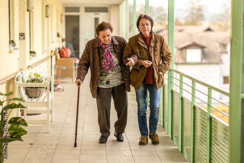 Elderly woman walking with support from her daughter, cane use and fall prevention outdoors