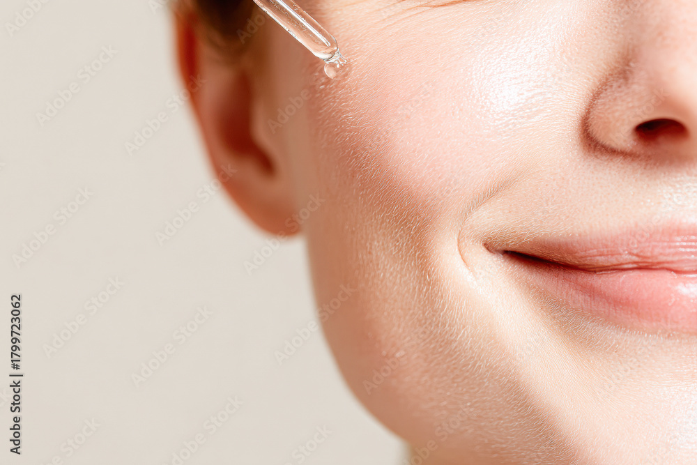 Obraz premium A close-up of a smiling woman's face applying skincare serum, highlighting healthy, glowing skin and a radiant complexion.