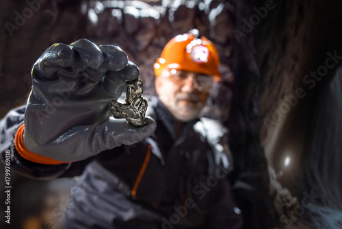 Foto Man in a hard hat with a flashlight holding metal nugget, rare earth metal