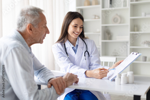 Smiling female doctor showing medical document to senior male patient during consultation in clinic office, positive healthcare communication and trust concept
