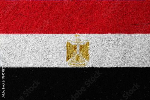 Textured depiction of the Egyptian national flag, showcasing the red, white, and black horizontal bands, with a golden Eagle of Saladin emblem centered, creating a nationalistic and