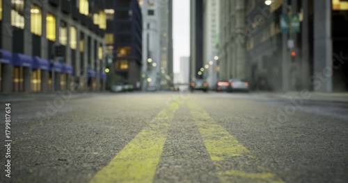 Dusk falls over a bustling city street, where vehicles move steadily along yellow lines. Buildings rise high on either side, reflecting the last light of day with windows aglow.