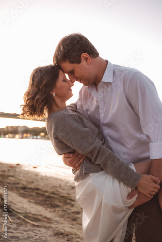 Joyful Couple Embracing on a Beach at Sunset with Warm Light and Urban Waterfront Background