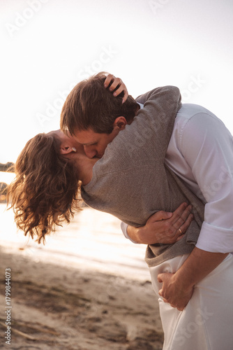 Joyful Couple Embracing on a Beach at Sunset with Warm Light and Urban Waterfront Background