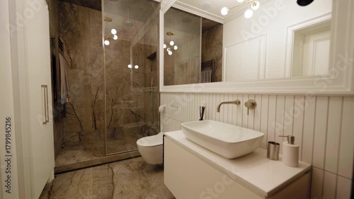 Elegant modern bathroom with large stone-tile shower area, wall-mounted toilet, minimalist white vanity, oversized mirror and warm ambient lighting