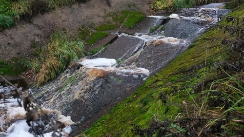 Stormy sewage flows down a cascade of concrete slabs with foam and hissing. A muddy stream.