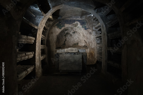 Dimly lit ancient catacomb chamber with stone shelves, altar and fresco fragments - atmospheric underground crypt in Naples, Italy