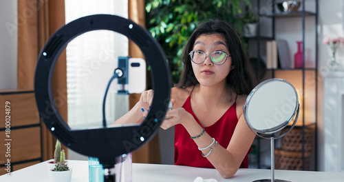 Female content creator records video blog, spreading face cream while explaining her skincare routine. She discusses beauty treatments with clarity and warmth.