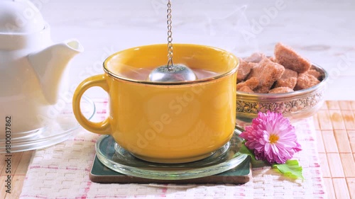 Black tea in a light cup on a table, against a light background, is brewed using a metal strainer.