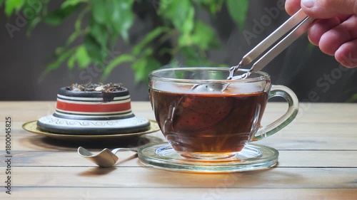 Black tea in a light cup on a table, against a light background, is brewed using a metal strainer.