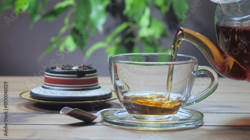 Black tea is poured into a light-colored cup from a teapot.