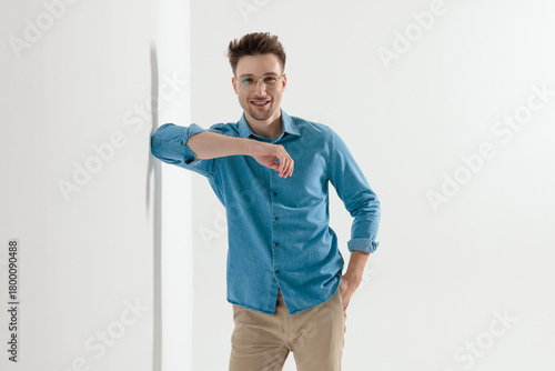 Happy young casual man smiling and leaning elbow on wall