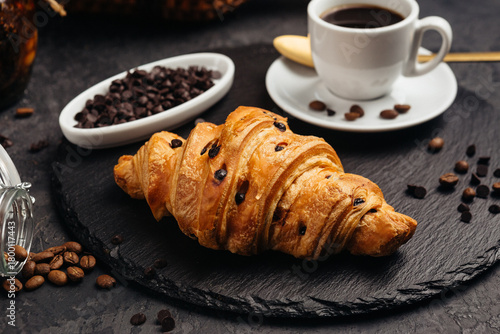 Фотография A large airy croissant with chocolate on a dark background tempts coffee