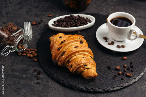 A large airy croissant with chocolate on a dark background tempts coffee