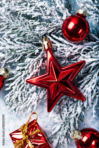 Festive Christmas composition with red holiday ornaments, including a shiny star-shaped decoration, red baubles, and a small gift box placed on snowy pine branches.