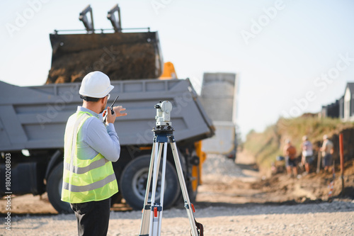 Canvas Print Engineer surveying construction site with dump truck operating