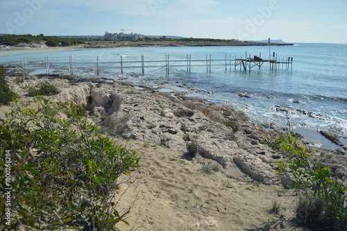 Coastal view with rocky shoreline and wooden pier under bright sky, serene nature landscape, copy space