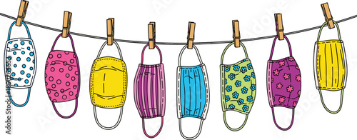 Assorted colorful cloth face masks with patterns hanging on a clothesline with clothespins
