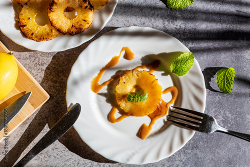 Grilled pineapple slices arranged with fresh mandarin segments and lemon pieces, creating a vibrant and refreshing tropical composition. The caramelized edges of the pineapple add warmth and texture, 