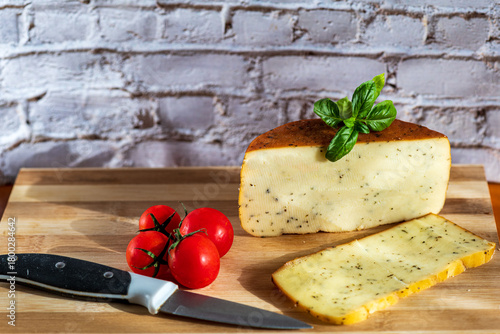 Sliced kulen and semi-hard cheese arranged neatly on a plate, garnished with fresh basil leaves. The vibrant colors of the red cured sausage, creamy-yellow cheese, and green basil create a visually ap